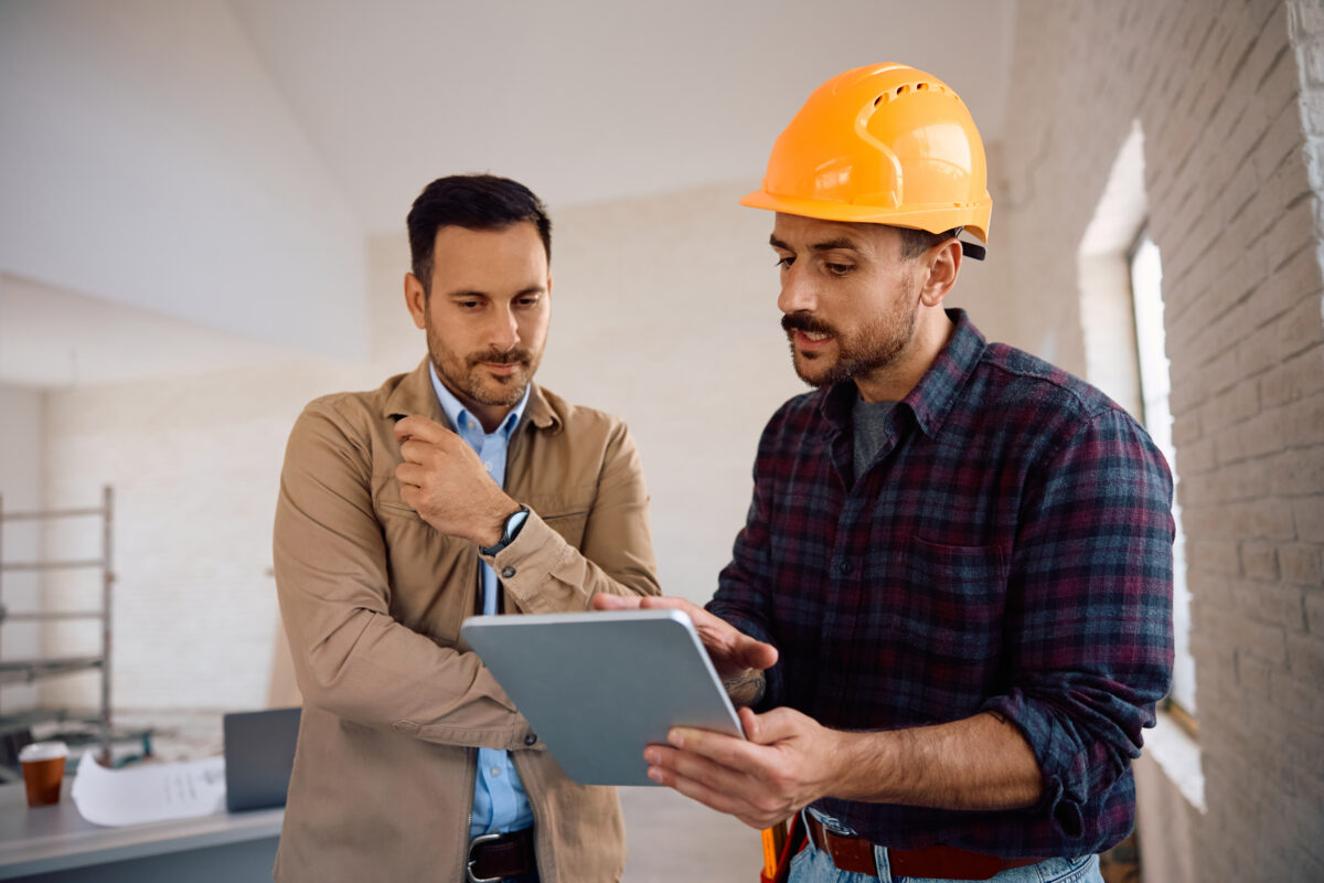 Construction worker using digital tablet with home owner during renovating process.