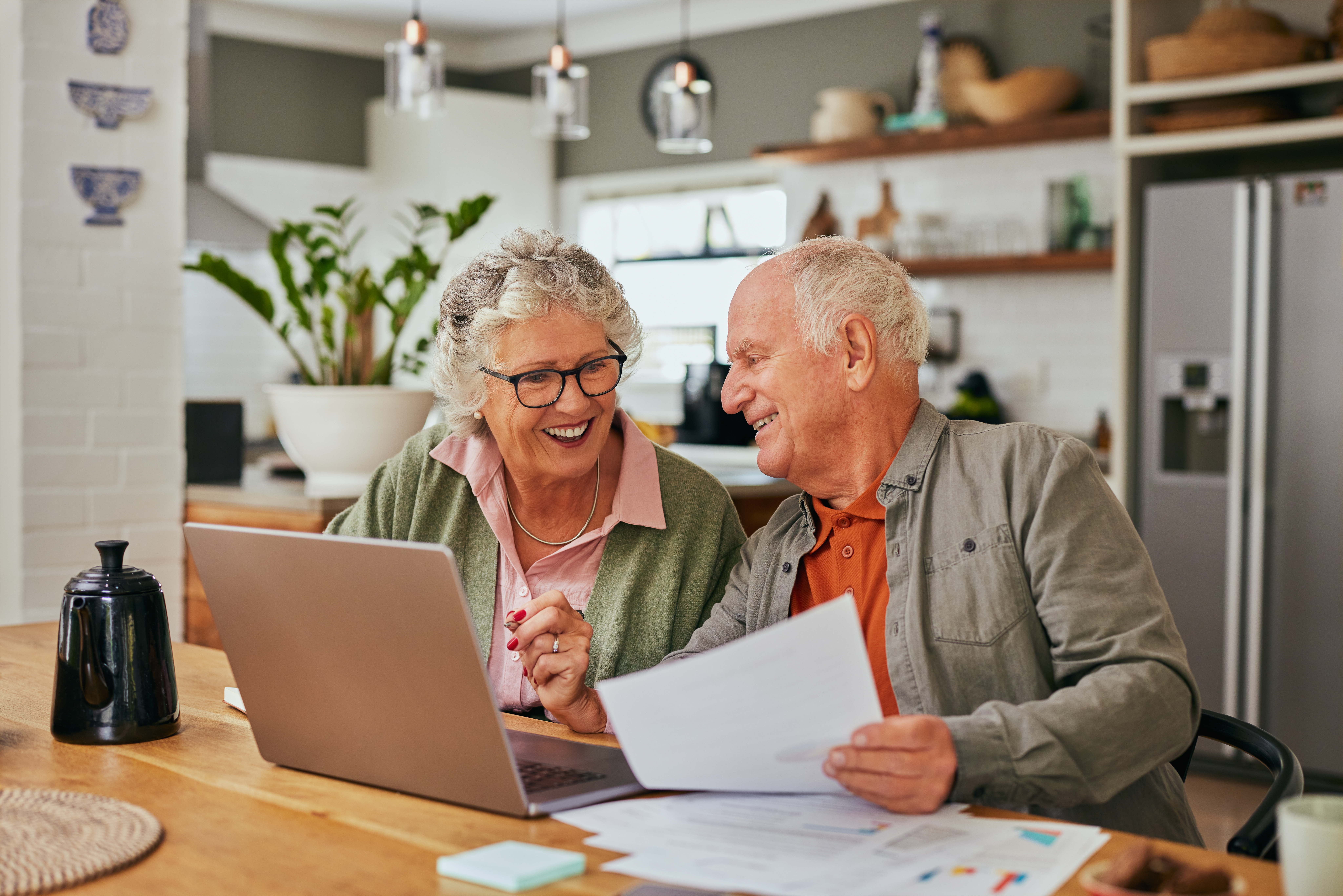 Un couple de retraités examine des documents financiers devant un ordinateur portable