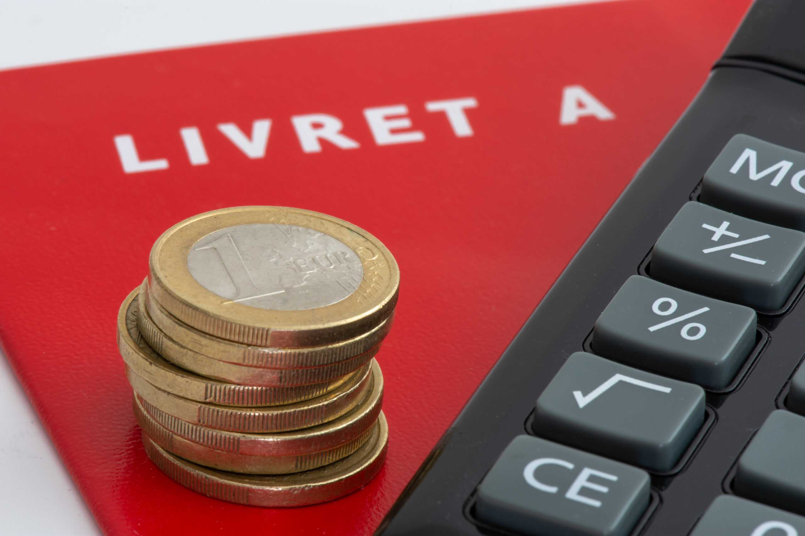 Un Livret A rouge, une pile de pièces en euros et une calculatrice.