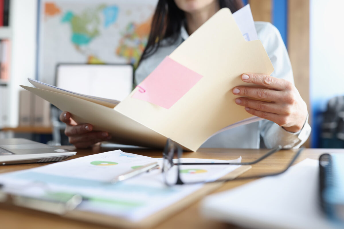 Une femme consulte un dossier papier à son bureau.