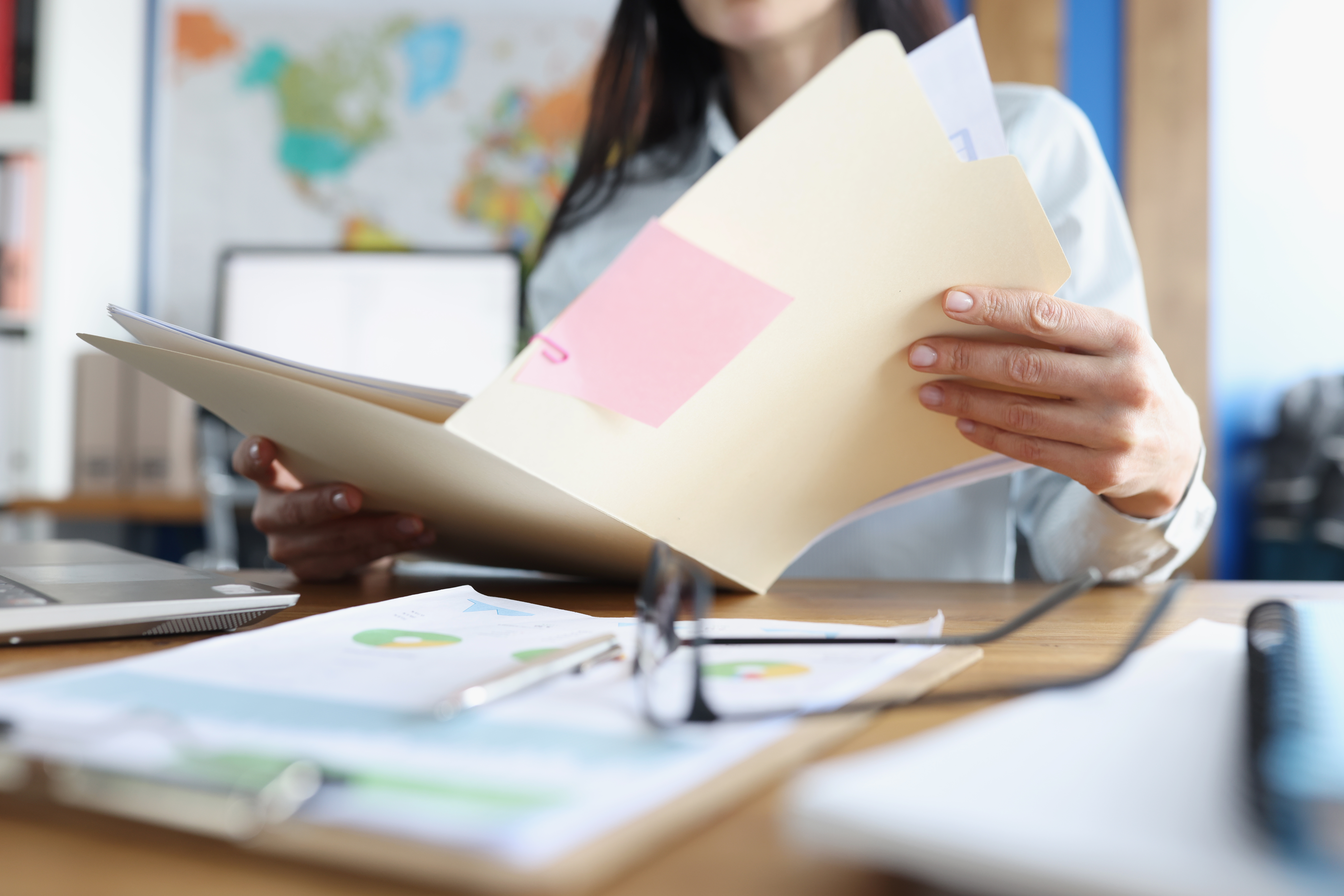 Une femme consulte un dossier papier à son bureau.