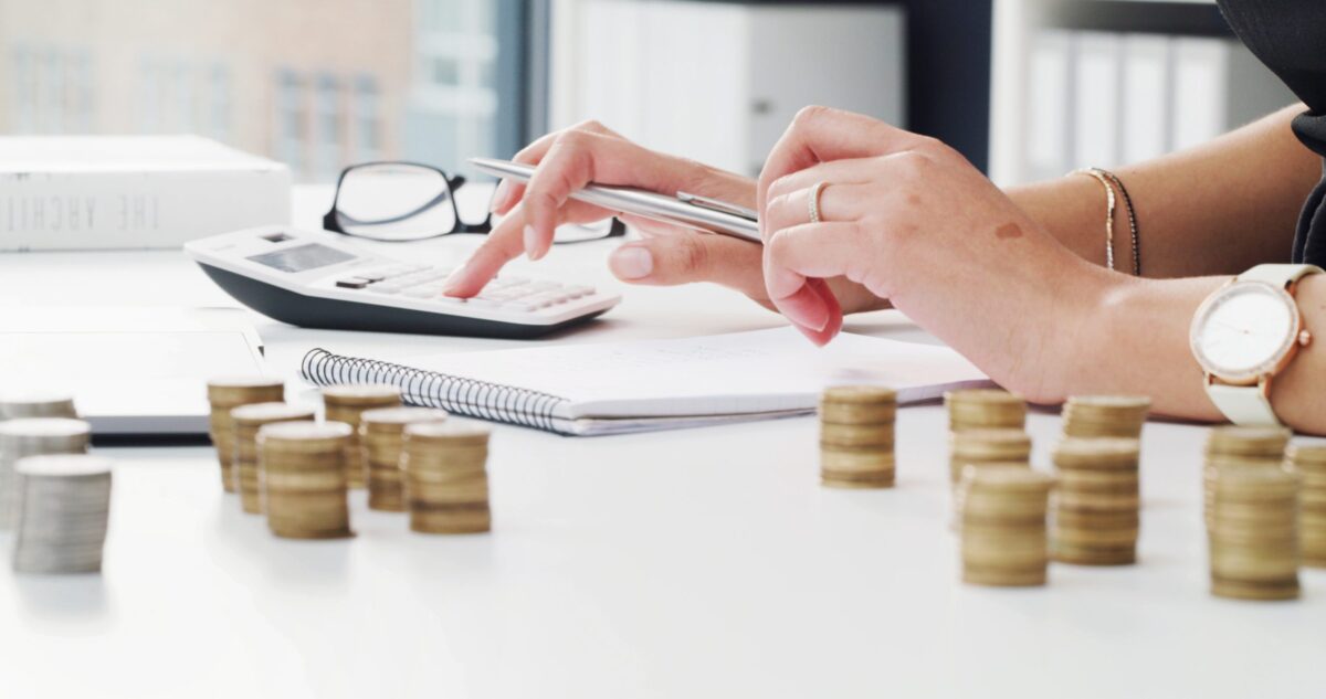 Mains utilisant une calculatrice sur un bureau avec des piles de pièces